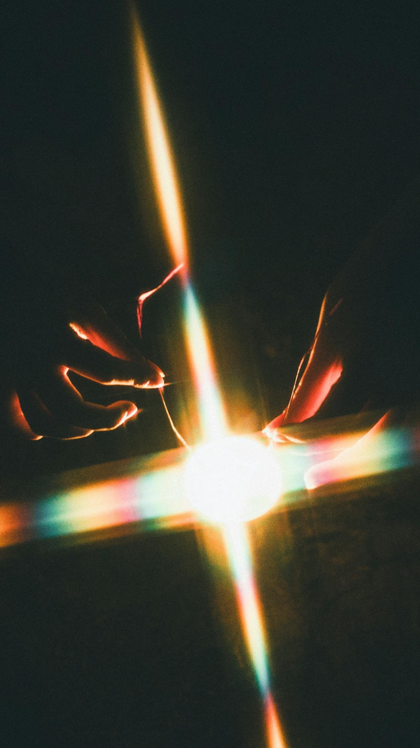 Hands creating an artistic light effect with rainbow colors in a dark setting.